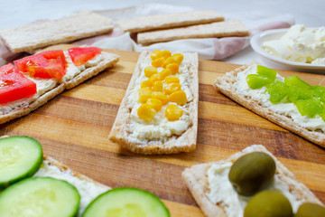 Homemade Crispbread toast with Cottage Cheese and green olives,slices of cabbage,tomatoes,corn,green pepper on cutting board on white concrete background.Healthy food concept,Top view.Flat Lay