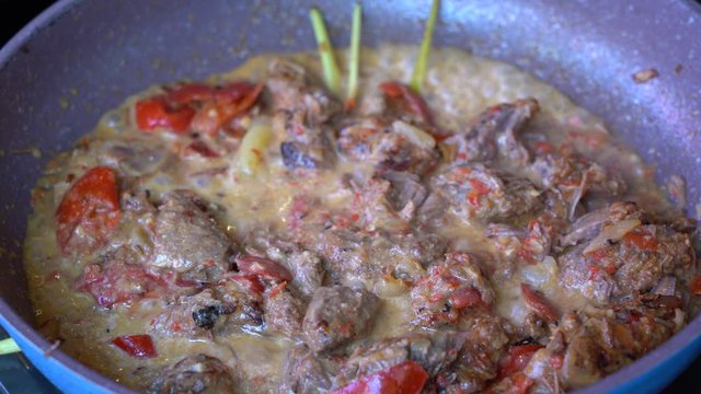 Frying pan with onion, lemongrass, red pepper and beef meat, close up. Indonesia. Sambal Goreng Ati Kentang, Indonesian cuisine, spicy beef meet and potatoes garnish with lemongrass leaf and red chili