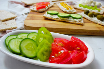 Homemade Crispbread toast with Cottage Cheese and green olives,slices of cabbage,tomatoes,corn,green pepper on cutting board on white concrete background.Healthy food concept,Top view.Flat Lay