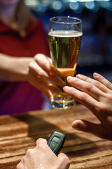 The bartender's hand at the bar holds out a beer in a glass. Man refuses with a gesture of his hand. In his left hand he holds the keys to the car.