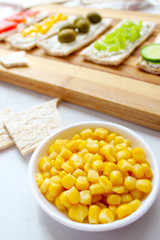 Homemade Crispbread toast with Cottage Cheese and green olives,slices of cabbage,tomatoes,corn,green pepper on cutting board on white concrete background.Healthy food concept,Top view.Flat Lay