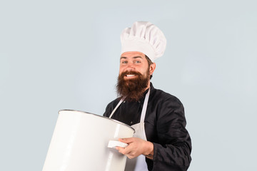 Cook man in apron holds saucepan in kitchen. Cookware, dinnerware, kitchenware. Cooking pot,...