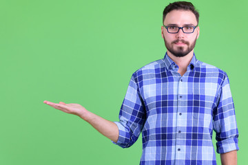 Young handsome bearded hipster man showing something