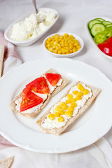 Homemade Crispbread toast with Cottage Cheese and green olives,slices of cabbage,tomatoes,corn,green pepper on cutting board on white concrete background.Healthy food concept,Top view.Flat Lay