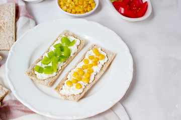 Homemade Crispbread toast with Cottage Cheese and green olives,slices of cabbage,tomatoes,corn,green pepper on cutting board on white concrete background.Healthy food concept,Top view.Flat Lay