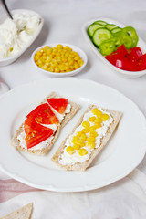 Homemade Crispbread toast with Cottage Cheese and green olives,slices of cabbage,tomatoes,corn,green pepper on cutting board on white concrete background.Healthy food concept,Top view.Flat Lay