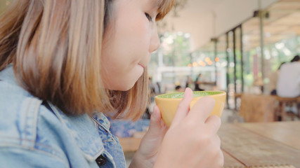 Business freelance Asian woman drinking warm cup of green tea or coffee while sitting on table in cafe. Lifestyle smart beautiful female relax in coffee shop concepts.