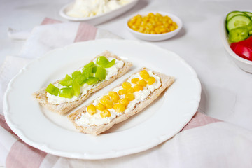 Homemade Crispbread toast with Cottage Cheese and green olives,slices of cabbage,tomatoes,corn,green pepper on cutting board on white concrete background.Healthy food concept,Top view.Flat Lay