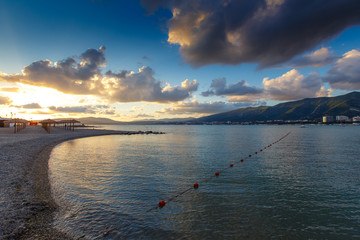 Naklejka na ściany i meble The Resort Of Gelendzhik. Sunset in Gelendzhik Bay. In the foreground pebble beach, the sea are fishing nets. further visible sun umbrellas and the sunset. Beautiful clouds. There are no people, the e