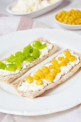Homemade Crispbread toast with Cottage Cheese and green olives,slices of cabbage,tomatoes,corn,green pepper on cutting board on white concrete background.Healthy food concept,Top view.Flat Lay