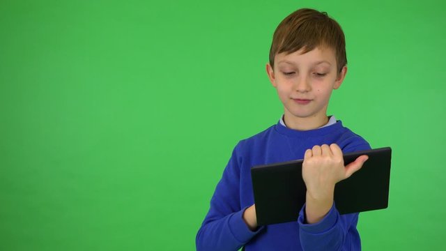A young cute boy works on a tablet - green screen studio