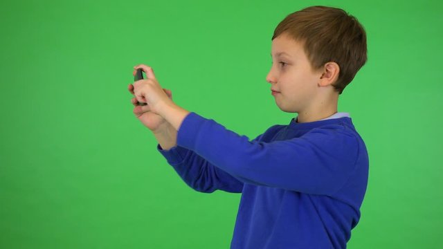A young cute boy takes pictures with a smartphone - green screen studio