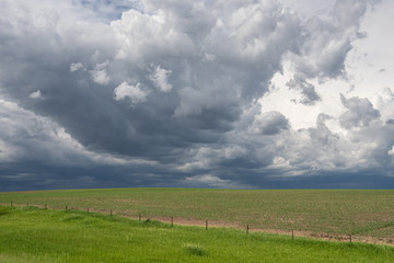 Landscape with dark storm clouds building in the sky over a recently planted field with a barbed wire fence during spring on North America’s Great Plains.