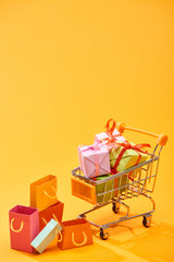 shopping cart with presents near shopping bags on bright orange background