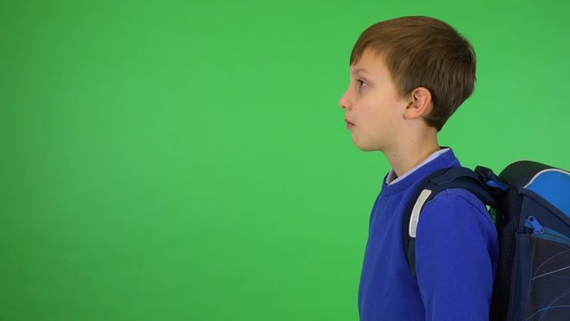 A young cute boy with a schoolbag turns to the camera and smiles - green screen studio