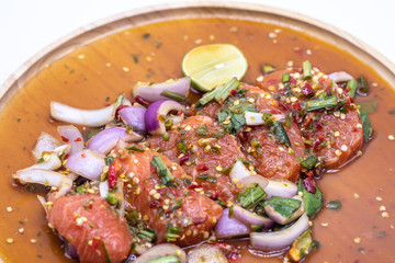 Thai spicy salmon salad in wooden plate isolate on white background.