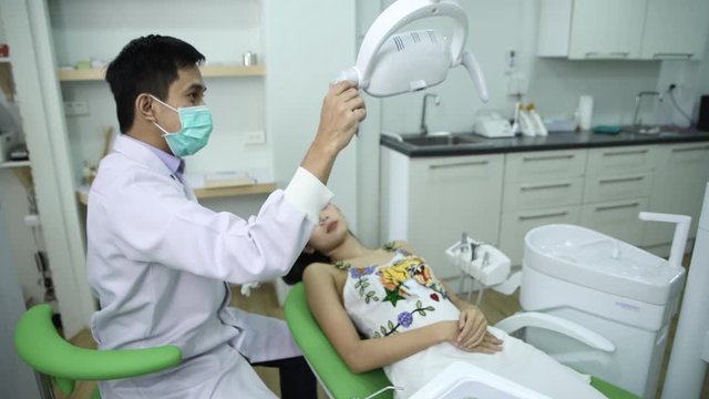 male dentist in dental office talking with female patient and preparing for treatment.