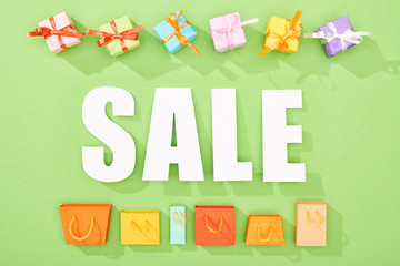top view of decorative gift boxes and shopping bags on green background with sale lettering