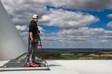 young male worker standing on top of a wind turbine with cloudy sky in the background