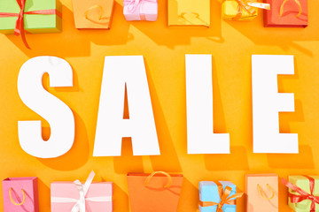 top view of white sale lettering near shopping bags and presents on bright orange background
