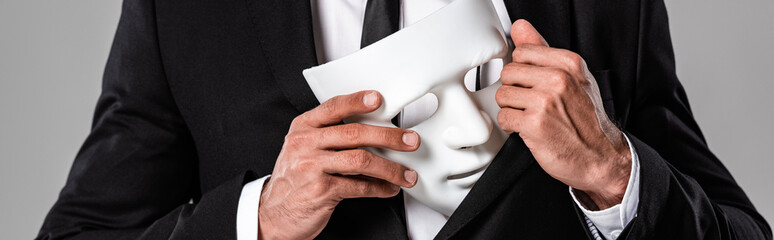 cropped view of businessman in black suit holding white mask isolated on grey, panoramic shot