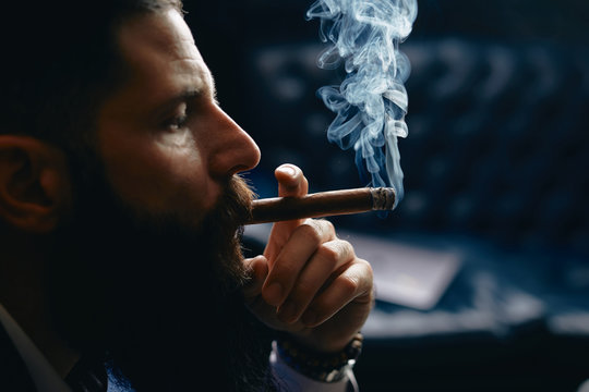Handsome Man with beard in suit lighting cuban cigar.