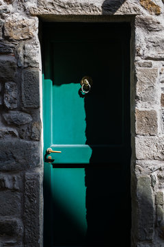 A green door against a stone wall that is half illuminated by sunlight.