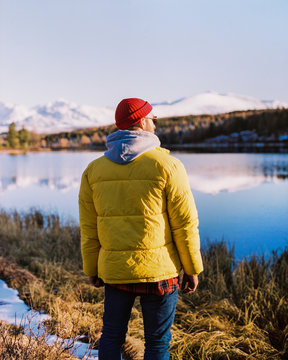 a young guy in a yellow jacket is standing on the shore of a lake. winter mountain landscape