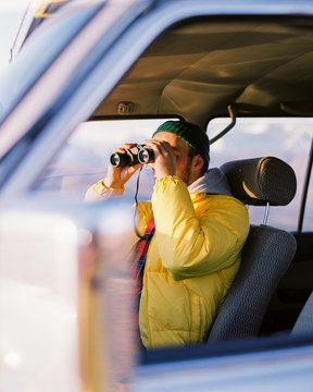 young guy the driver is sitting in the car and looking through binoculars