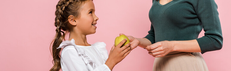 panoramic shot of mother giving tasty apple to cute daughter isolated on pink
