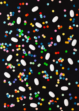 Pills and confetti scattered on a black background