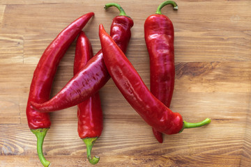 Five red hot chili peppers on a brown wooden background, top view