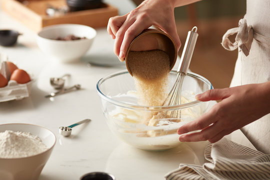 Cook pouring brown sugar in dough.