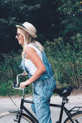 Beautiful blonde teenage girl happily riding bicycle through the forest or park. Closeup.