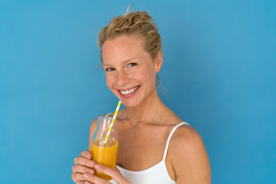 Smiling blond woman drinking juice, blue background
