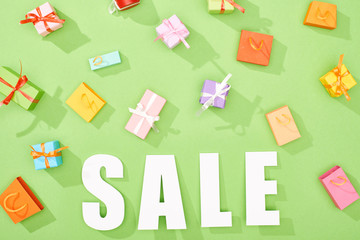 top view of scattered decorative gift boxes and shopping bags on green background with sale word