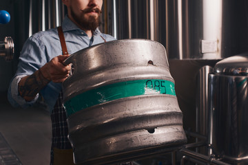 Brewery worker adds more beer to the bigger barrel from smaller one.