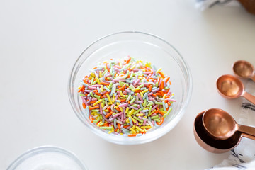 cake ingredients on white background, rainbow sprinkles in bowl