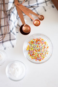 cake ingredients on white background, rainbow sprinkles in bowl