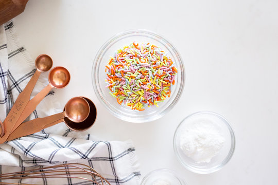 cake ingredients on white background, rainbow sprinkles in bowl