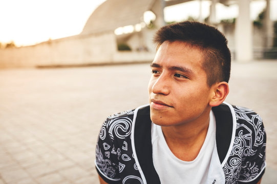 Portrait of hispanic young break dancer seated in urban park at sunset