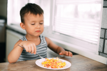 a child in a t-shirt in the kitchen eating an omelet with sausage and tomatoes