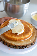 woman icing vanilla cake with metal spatula 