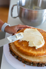 woman icing vanilla cake with metal spatula 