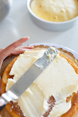 woman icing vanilla cake with metal spatula 