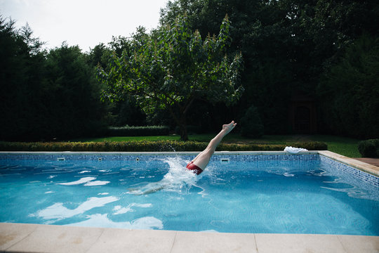 Young Man Jumping In Swimming Pool In The Garden. Healthy Lifestyle. Side View