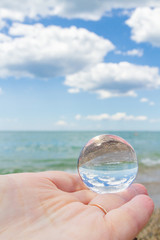 The glass round ball on the hand reflects the beach in the summer