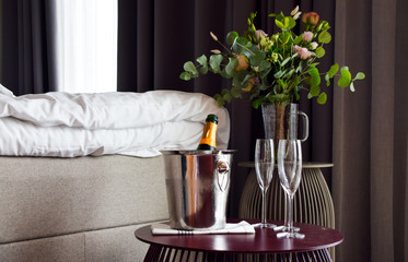 Romantic setting in the bedroom with open champagne bottle and empty champagne glasses on table in...