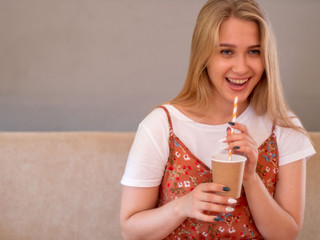 Slender charming young blonde in white T-shirt and colorful sundress poses in front of camera in studio with environmentally friendly cardboard cup, dishes and cocktail tube. Nature protection concept
