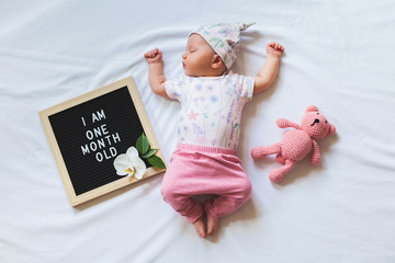 Portrait of sleeping one month old newborn baby girl laying between letter board and teddy bear....